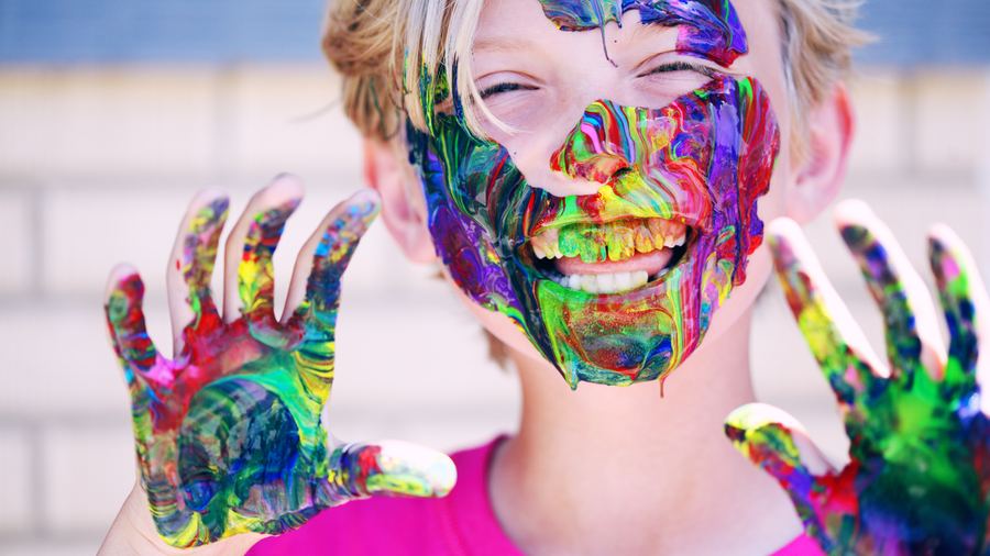 A child with paint covering their hands and face, grinning at the camera